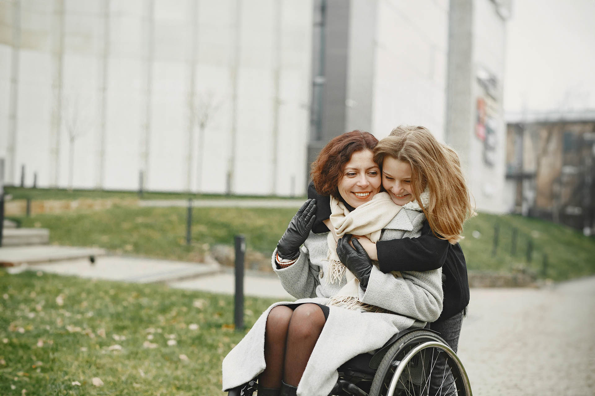 All'aperto, mamma in sedia rotelle con figlia adolescente che l'abbraccia - Sostegno sclerosi multipla